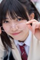 A young woman in a school uniform holding up a pair of glasses.