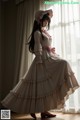 A woman in a long dress and hat sitting on a window sill.