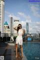 A woman in a white dress standing next to a swimming pool.