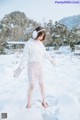 A woman in a white sweater and skirt standing in the snow.