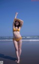 A woman in a yellow bikini and straw hat on the beach.