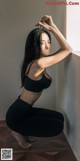 A woman in a black bra top and black leggings leaning against a wall.