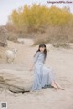 A woman in a blue dress sitting on a log in the sand.