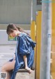 A woman sitting on a ledge in a blue shirt dress.