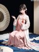 A woman in a pink and white kimono sitting on a bed.