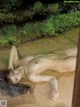 A naked woman laying on a bamboo mat in a garden.