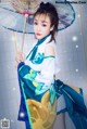 A woman in a blue and green dress holding an umbrella.