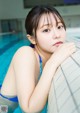 A woman in a blue bikini leaning against a wall in a pool.